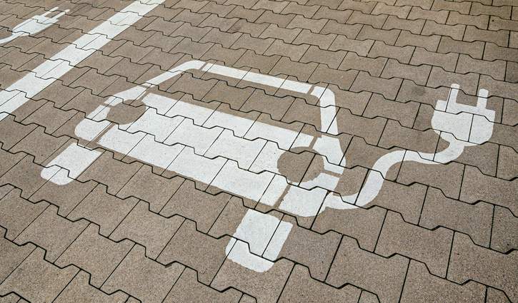Markierung eines E‑Auto‑Parkplatzes auf Pflastersteinen mit weißem Symbol eines Elektrofahrzeugs und Ladesteckers