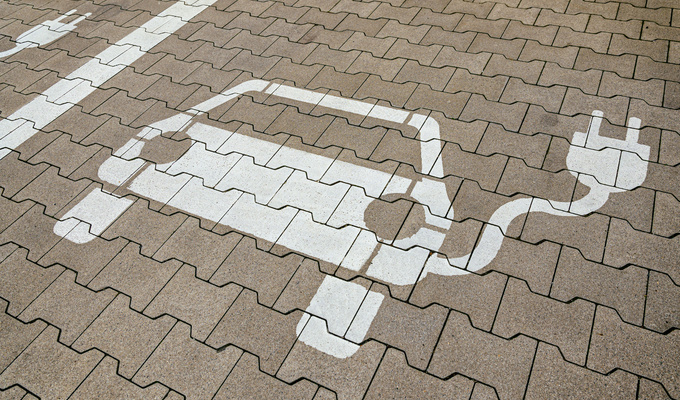 Markierung eines E‑Auto‑Parkplatzes auf Pflastersteinen mit weißem Symbol eines Elektrofahrzeugs und Ladesteckers