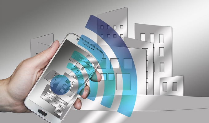 Hand hält ein Smartphone, aus dem ein blaues WLAN-Symbol hervorgeht; im Hintergrund stilisierte Gebäudegrafiken